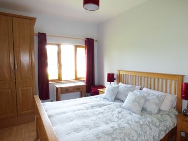 A bedroom with a wooden bed and wardrobe near a window with red curtains at Maifield in Carrick-On-Suir County Tipperary