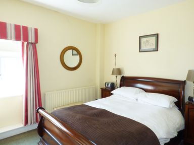 A bedroom with a wooden bed, bedside tables with lamps, a round mirror on the wall and curtains at Maifield in Carrick-On-Suir County Tipperary