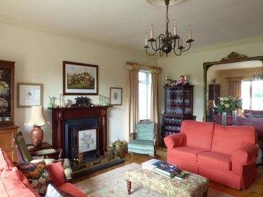 A living room with red sofas a fireplace a chandelier a large mirror and a glass cabinet at Maifield in Carrick-On-Suir County Tipperary