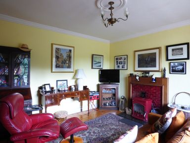 A living room with a red leather armchair a wooden desk and cabinet a television above a wooden shelf and a fireplace with red tiles at Maifield in Carrick-On-Suir County Tipperary