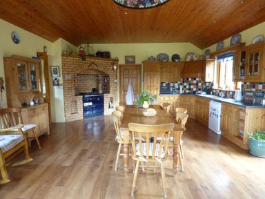 A kitchen with a wooden dining table and chairs a brick oven wooden cabinets and tiled backsplash at Maifield in Carrick-On-Suir County Tipperary