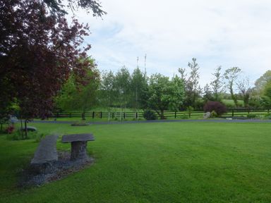 A grassy garden with stone bench and table near trees and a wooden fence at Maifield in Carrick-On-Suir County Tipperary