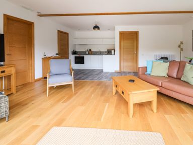 A living room with a brown sofa with cushions a wooden coffee table a blue armchair and a kitchen area at No1 The Lodge in Acton near Bishops Castle