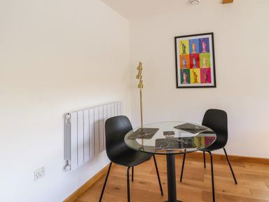 A dining area with a round glass table and two black chairs with a colorful framed artwork on the wall at No1 The Lodge in Acton near Bishops Castle