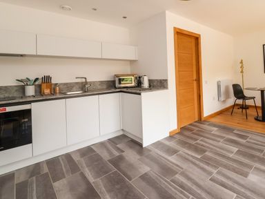 A modern kitchen with white cabinets grey tiled floor wooden door and a chair with a table at No1 The Lodge in Acton near Bishops Castle
