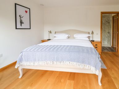 A bedroom with a bed between two wooden nightstands and a door leading to a bathroom at No1 The Lodge in Acton near Bishops Castle