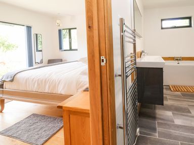 A bedroom with a bed and a mirror next to a bathroom with a sink and a bathtub at No1 The Lodge in Acton near Bishops Castle