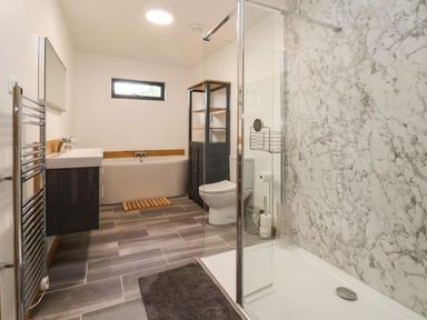 A bathroom with a shower area featuring marble walls a toilet a bathtub a sink with a mirror and a towel rail at No1 The Lodge in Acton near Bishops Castle