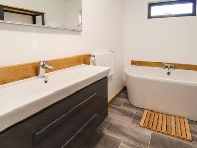 A bathroom with a sink vanity unit a bathtub and a wooden bath mat at No1 The Lodge in Acton near Bishops Castle
