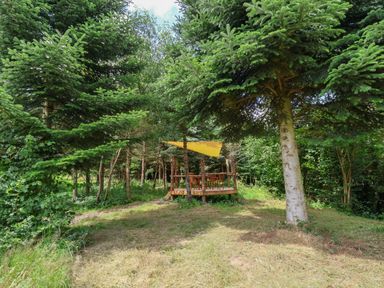 An outdoor wooden deck with a table and chairs under a yellow canopy surrounded by trees at No1 The Lodge in Acton near Bishop's Castle