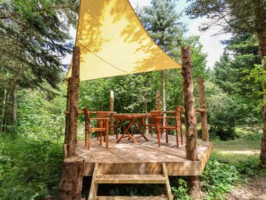 An outdoor wooden deck with a table and four chairs under a yellow canopy surrounded by trees at No1 The Lodge in Acton near Bishops Castle