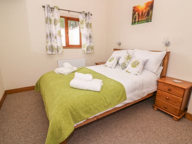 A bedroom with a wooden double bed green blanket floral cushions wooden bedside tables and curtains at Pentre Fach in Llandrindod Wells