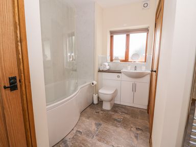 A bathroom with a bathtub shower, toilet, sink with cabinet, and a window at Pentre Fach in Llandrindod Wells