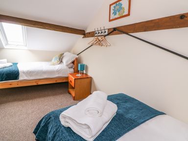 A bedroom with two single beds a wooden nightstand with a lamp wooden hangers on wall hooks and a slanted ceiling at Pentre Fach in Llandrindod Wells