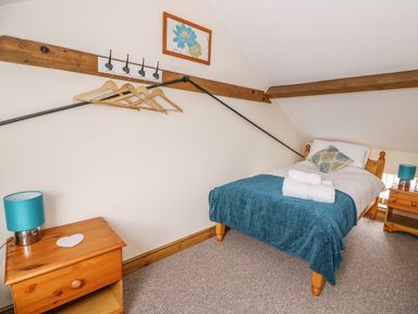 A bedroom with a single bed covered with a blue throw and folded towels with a pillow two wooden bedside tables each with a lamp and a wall-mounted coat rack with hangers at Pentre Fach in Llandrindod Wells