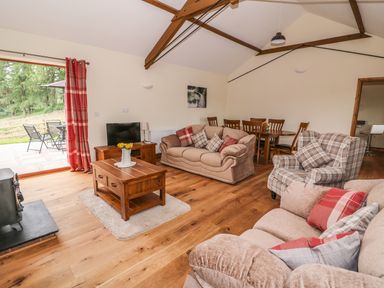 A living room with sofas cushions a wooden coffee table tv and a dining table with chairs at Pentre Fach in Llandrindod Wells