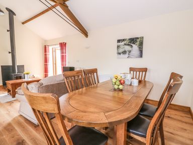 A dining table with six chairs and a fruit basket in a living room with a sofa a wood stove and red curtains at Pentre Fach in Llandrindod Wells