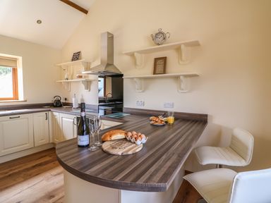 A kitchen with a wooden countertop with bread eggs and orange juice and two white chairs at Pentre Fach in Llandrindod Wells