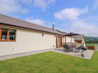 A patio with outdoor table chairs umbrella and barbecue beside a grass lawn at Pentre Fach in Llandrindod Wells