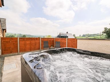 An outdoor hot tub with water jets and two chairs with a table behind it at Pentre Fach in Llandrindod Wells