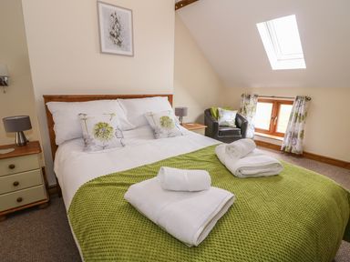 A bedroom with a double bed and green bedspread with rolled white towels on the bed at Pentre Fawr in Llandrindod Wells