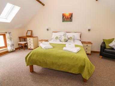 A bedroom with a double bed covered with a green blanket and white pillows bedside tables a dressing table and a black armchair at Pentre Fawr in Llandrindod Wells