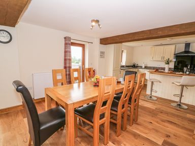 A dining area with a wooden table and chairs next to a kitchen with cream cabinets and bar stools at Pentre Fawr in Llandrindod Wells