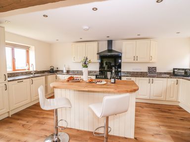 A kitchen with an island counter with food and flowers and two white bar stools at Pentre Fawr in Llandrindod Wells