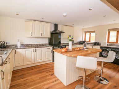 A kitchen with cream cabinets a wooden floor an island with stools and windows at Pentre Fawr in Llandrindod Wells