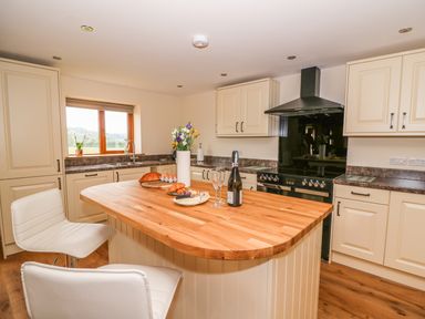 A kitchen with cream cabinets wooden countertop island white chairs and food items at Pentre Fawr in Llandrindod Wells