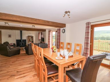 A dining area with a wooden table and chairs next to a living room with sofas and a fireplace at Pentre Fawr in Llandrindod Wells