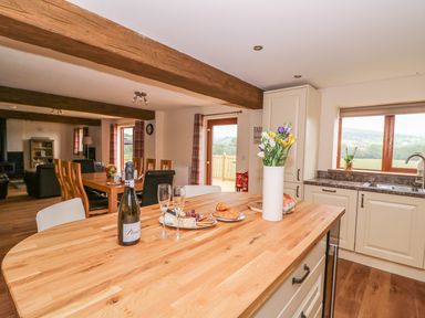 A kitchen with an island counter with flowers and a bottle of prosecco a dining table and living area with wooden beams at Pentre Fawr in Llandrindod Wells