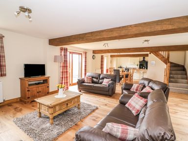 A living room with brown leather sofas and a wooden coffee table with flowers at Pentre Fawr in Llandrindod Wells