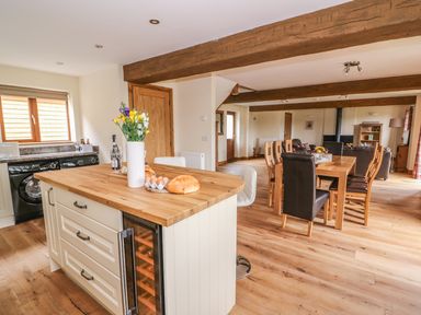 A kitchen island with a vase of flowers and bread next to a dining table with chairs in a room with wooden beams at Pentre Fawr in Llandrindod Wells