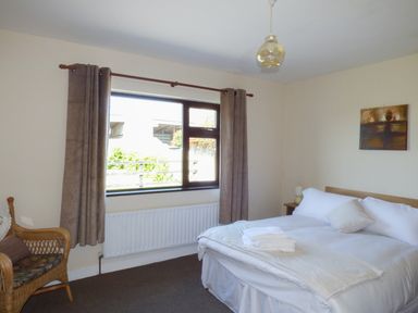 A bedroom with a double bed bedside table wicker chair window with curtains and a painting on the wall at Nephin View in Foxford County Mayo