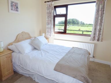 A bedroom with a double bed white bedding bedside tables lamps a window with floral curtains and a view of green fields at Nephin View in Foxford County Mayo