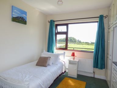 A bedroom with a single bed a nightstand a lamp blue curtains and a window showing a green field at Nephin View in Foxford County Mayo