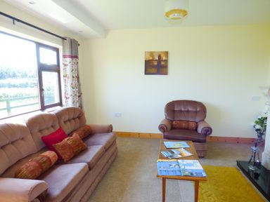 A living room with sofa and armchair a wooden coffee table and window with floral curtains at Nephin View in Foxford County Mayo