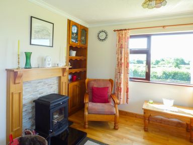 A living room with an armchair by a wood stove and a window at Nephin View in Foxford County Mayo