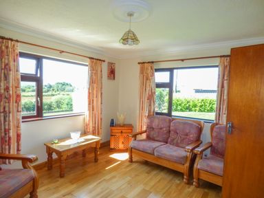 A sitting room with wooden furniture including a sofa armchair and coffee table and two large windows at Nephin View in Foxford County Mayo