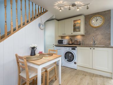 A kitchen with a wooden dining table and chairs under a staircase with white paneling and a washing machine at Rose Cottage in Edlingham