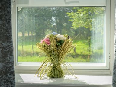 A bouquet of flowers tied with straw placed on a window sill with greenery visible outside at Rose Cottage in Edlingham