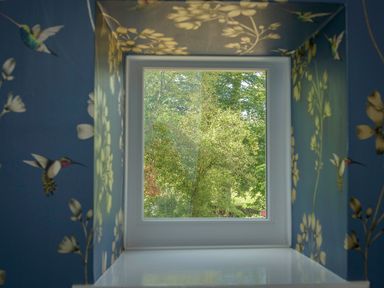 A window with a view of trees framed by blue wallpaper with birds and flowers at Rose Cottage in Edlingham