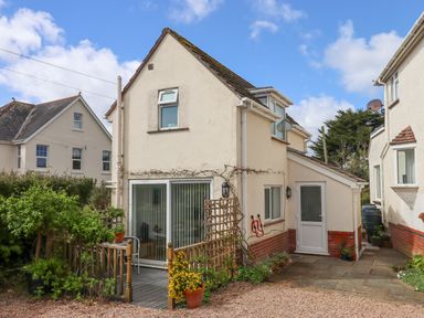 The back of a two story cream house with a wooden deck and potted plants at Wisteria Cottage in Exmouth