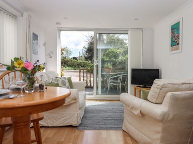 A living room with armchairs table with flowers television and sliding glass door leading outside at Wisteria Cottage in Exmouth