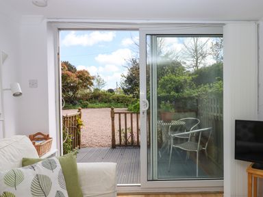 A living area opening to a garden through sliding glass doors with a small outdoor table and chairs at Wisteria Cottage in Exmouth