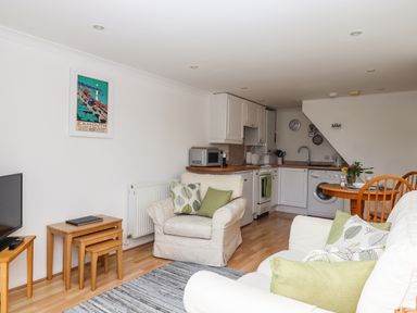 A living room with sofa and armchair next to a kitchen with white cabinets and wooden fixtures at Wisteria Cottage in Exmouth