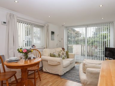 A living room with a wooden dining table and chairs two sofas and large windows with vertical blinds at Wisteria Cottage in Exmouth