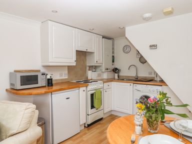A small kitchen with white cabinets a microwave a coffee machine an oven a sink and a washing machine at Wisteria Cottage in Exmouth