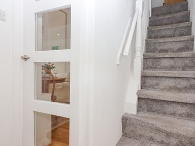 A carpeted staircase next to a white door with glass panels showing a dining area at Wisteria Cottage in Exmouth